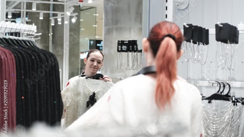 A sweet teenage girl looks in the mirror at a clothing store. She is trying on a prom dress, evaluating her appearance.