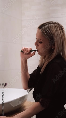Morning routine: A beautiful blonde brushing her teeth in the bathroom. Side view.