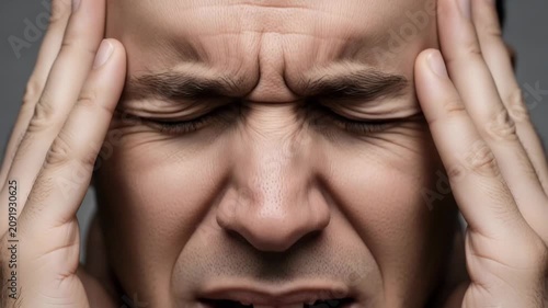 Intense Headache A close up shot captures a man grimacing with pain his eyes squeezed shut as he clutches his temples conveying the debilitating feeling of a severe headache