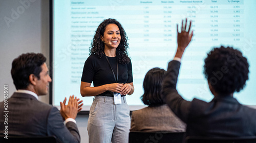 Tableau sur toile Joyful business woman with a microphone presenting data to an engaged audience at a corporate conference event