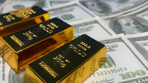 Stacked gold bars arranged on scattered one-hundred-dollar bills, illustrating asset accumulation and diversified financial holdings