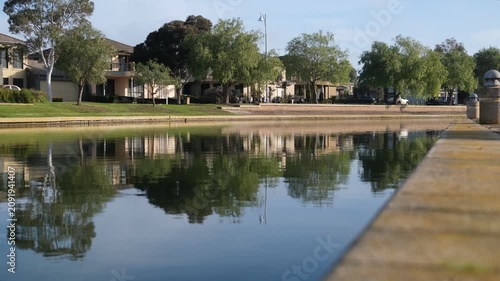 Tree-lined homes reflect on a still waterway at Sanctuary Lakes, Point Cook. Tranquil waterside living and desirable environment in suburban Melbourne, Australia.