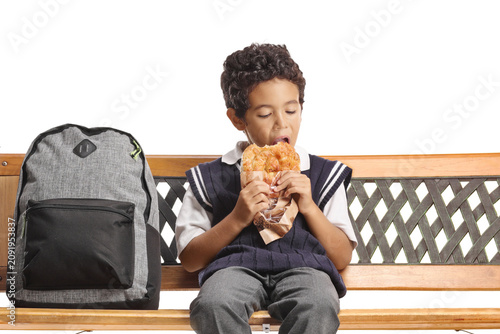 Quadro su tela Schoolboy sitting on a bench and eating a pastry for breakfast