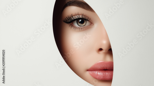 Close view of a woman's face behind a circular cut-out in a white surface during a beauty photoshoot