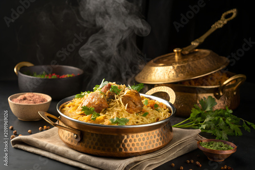 Traditional biryani served in a brass pot with saffron rice and herbs