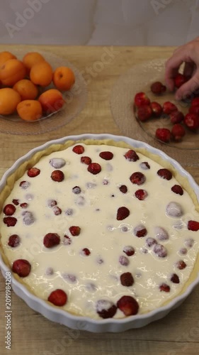 Woman's hands placing fresh strawberries on raw dough in a baking dish while preparing a pie