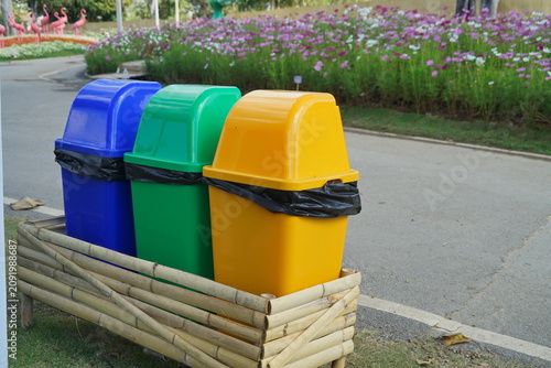 Colorful blue green and yellow recycling bins outdoors beside flower garden