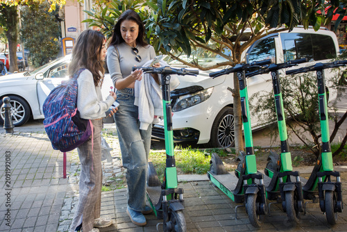 Obraz na plátně Two people discuss electric scooters on a city street with trees and cars in the