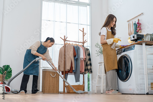 Woman laundry vacuum appliance home cleaning clothing basket window room with two people doing housework in bright interior calm domestic chore and fabric care scene