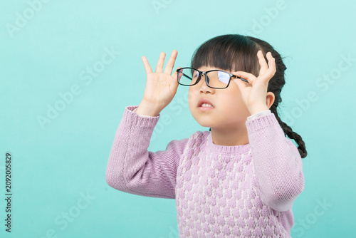 Fotografía Stressed little girl with glasses frowning and touching frames, eye strain and myopia concept, mint background