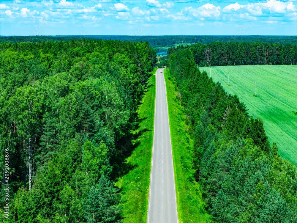 Naklejka premium Aerial view showcasing a long winding road bordered by lush green forests and fields