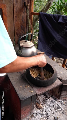Man manually roasting raw coffee beans in a clay pot over an open fire in a rustic setting