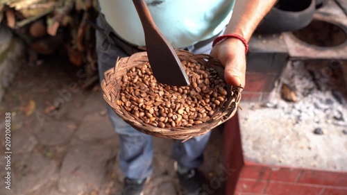 Male hands mixing roasted coffee beans with a wooden spoon in a wicker basket