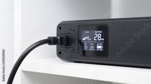A modern power management device is charging, displaying a battery percentage of 45 and a remaining runtime of 28 minutes. The sleek design fits neatly on a shelf, ideal for home use.