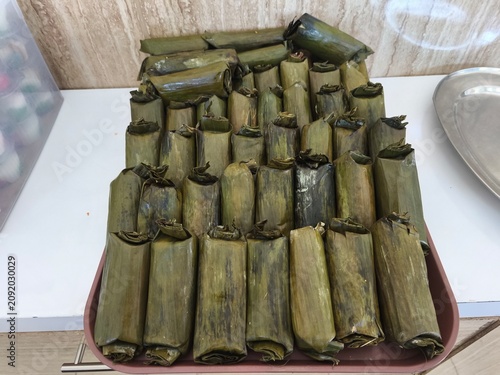A high-angle, close-up shot of numerous indonesian traditional snacks called arem-arem or lontong, neatly arranged on a tray, wrapped in green banana leaves and secured with toothpicks.