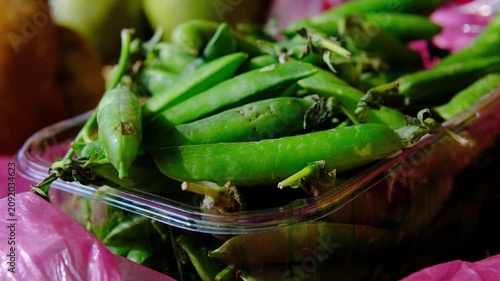 Fresh green pea pods in plastic container and pink bag at local farmers market, seasonal organic vegetables on display, healthy farm produce for everyday cooking and nutrition