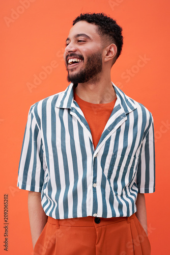 Smiling man wearing striped shirt standing against orange background