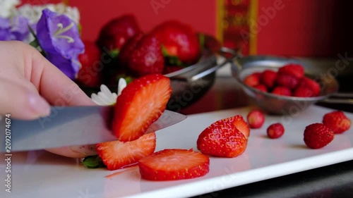 Female hands slicing fresh strawberries into thin slices on wooden cutting board for healthy breakfast, desserts and homemade recipes, preparing seasonal berries for serving