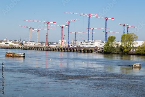 Ensemble de nombreuses grues rouges et bleues sur fond de ciel pour un chantier de construction de bâtiments au bord d'un fleuve. Ile de Nantes devant la Loire