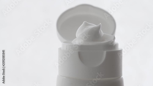 Close-up of hand and face cream in an open white plastic package on a neutral background.
