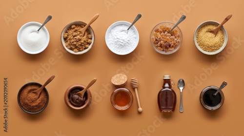 Assorted Natural Sweeteners and Sugars Arranged in Bowls and Jars on a Simple Brown Background