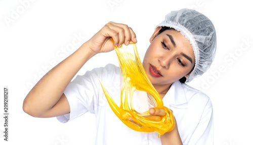 Focused Young Woman Stretching Yellow Slime While Wearing Lab Coat and Hair Net in Studio