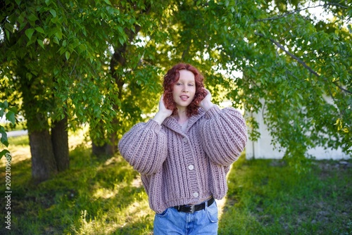 Young girl with curly red hair in chunky knit sweater with hood outdoors. Bulky knitwear, street fashion and style concept