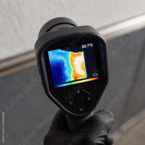Close up of handheld thermal imaging camera inspecting a building wall, vivid heat map display showing hot and cold zones for energy audit, insulation leak detection and maintenance