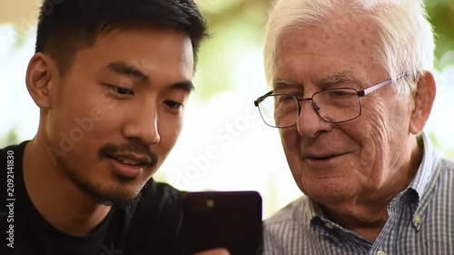 Young Man and Elderly Man Sharing a Smartphone Outdoors, Connecting