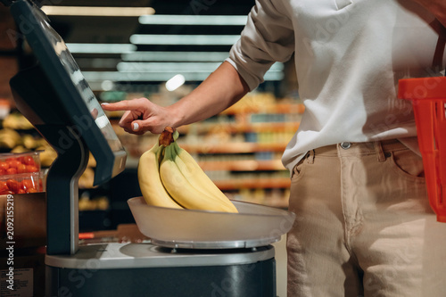 Individual weighing fresh bananas at self-service checkout in grocery store, showcasing modern shopping experience and healthy food choices
