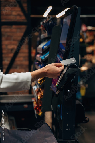 Hand of a customer using a credit card at a self-service checkout kiosk in a modern retail store, showcasing the convenience of digital payment technology