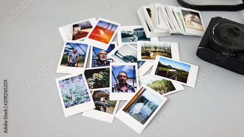Collection of instant photos spread out on a table next to a camera and some film stacks
