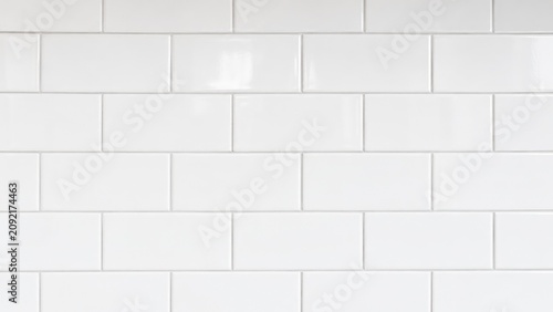 Glossy white subway tile wall with horizontal rectangular ceramic tiles and light gray grout, creating a clean modern kitchen or bathroom backsplash