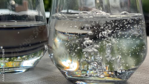 Pouring sparkling water into three drinking glasses at outdoor cafe table, refreshing beverage service before lunch, pizza and cocktails in summer restaurant