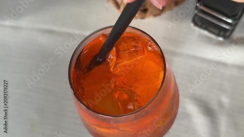 Glass of Aperol spritz cocktail with black straw on restaurant table, refreshing orange summer drink for outdoor cafe, social dining and relaxed evening atmosphere