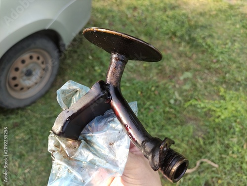 Foto Hand holding oil pump pick up tube with strainer, bottom view, car in background