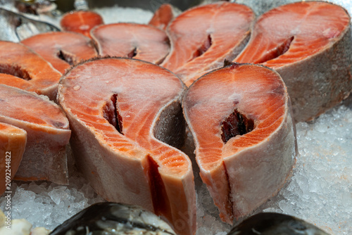 Frozen salmon steaks close up on ice bed inside supermarket display, fresh raw red fish cutlets for healthy diet food and seafood retail market advertisement