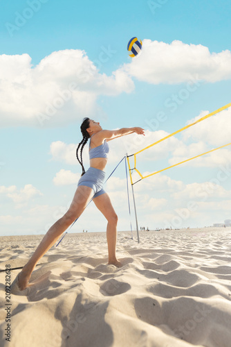 Beach volleyball player hits ball during game on sunny day near ocean in summertime