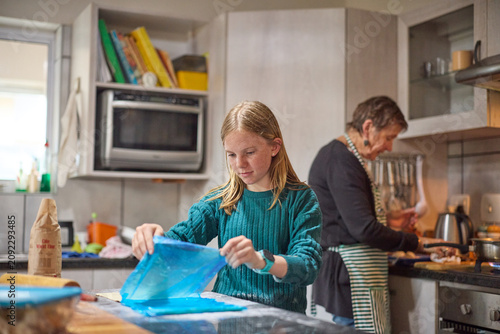 Young girl baking with her grandmother in a busy family kitchen, learning and smiling together
