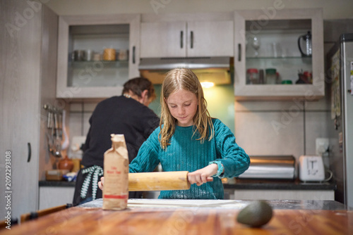 Young girl baking with her grandmother in a cozy home kitchen rolling dough together
