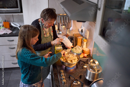 Grandmother and granddaughter baking together in a cozy home kitchen, teaching and sharing family recipes