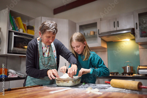 Grandmother and granddaughter baking together in a cozy home kitchen, sharing tradition and teaching