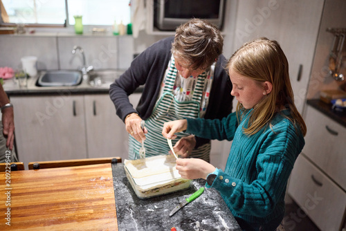 Grandmother and granddaughter baking together in a cozy family kitchen making layered pastry