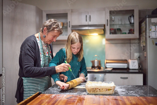 Grandmother teaching young girl to bake in cozy kitchen while preparing homemade pie
