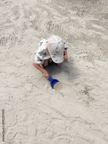 Fotografie Child digging with blue shovel in playground sand