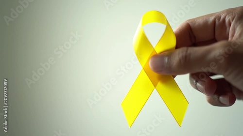 Hand holding yellow awareness ribbon for support and hope