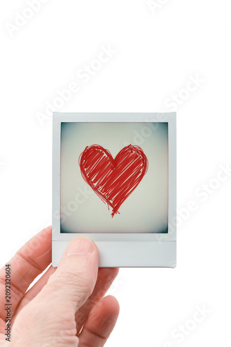 Inquadratura con mano in primo piano che regge una fotografia tipo istantanea con un cuore abbozzato in tratto rosso sfondo trasparente o bianco