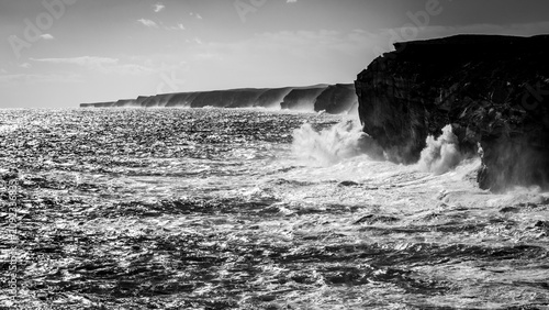 Powerful ocean swell hitting high cliffs on a rough coast, black and white landscape