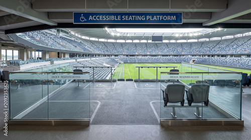 Accessibility infrastructure featuring a designated seating platform with glass partitions overlooking a professional sports stadium field.