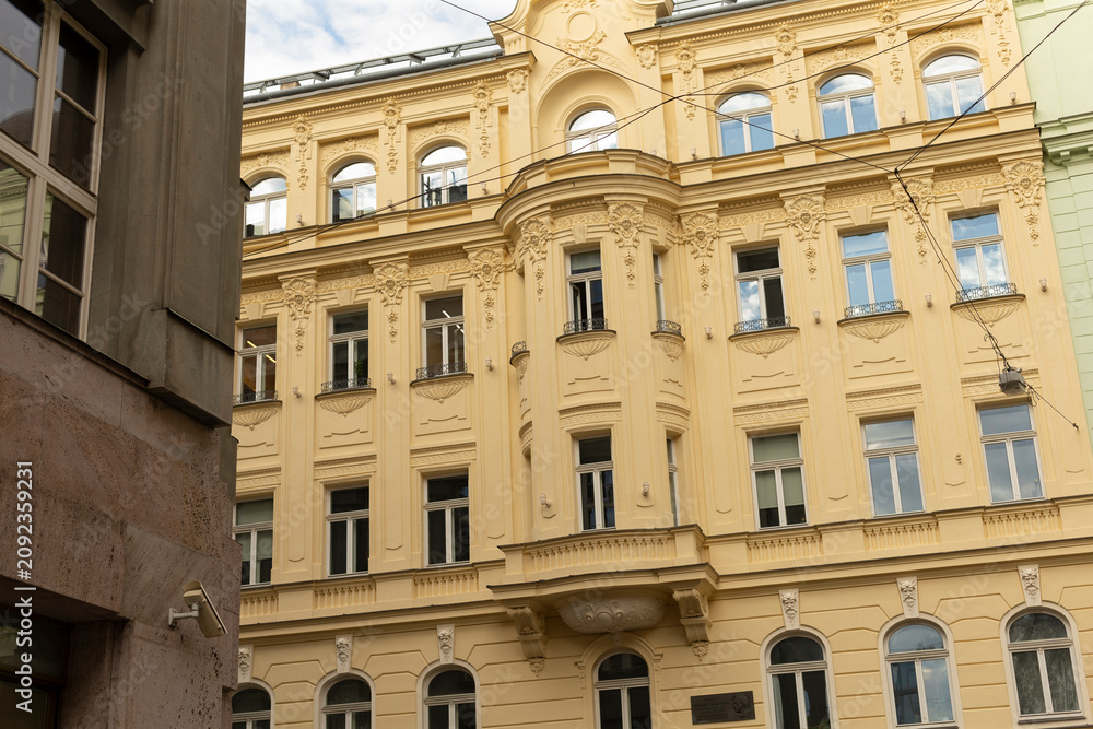 Obraz premium Facade of an ornate pale yellow historic apartment building showcasing decorative stucco, window cornices, arched ground-floor openings, small balconies